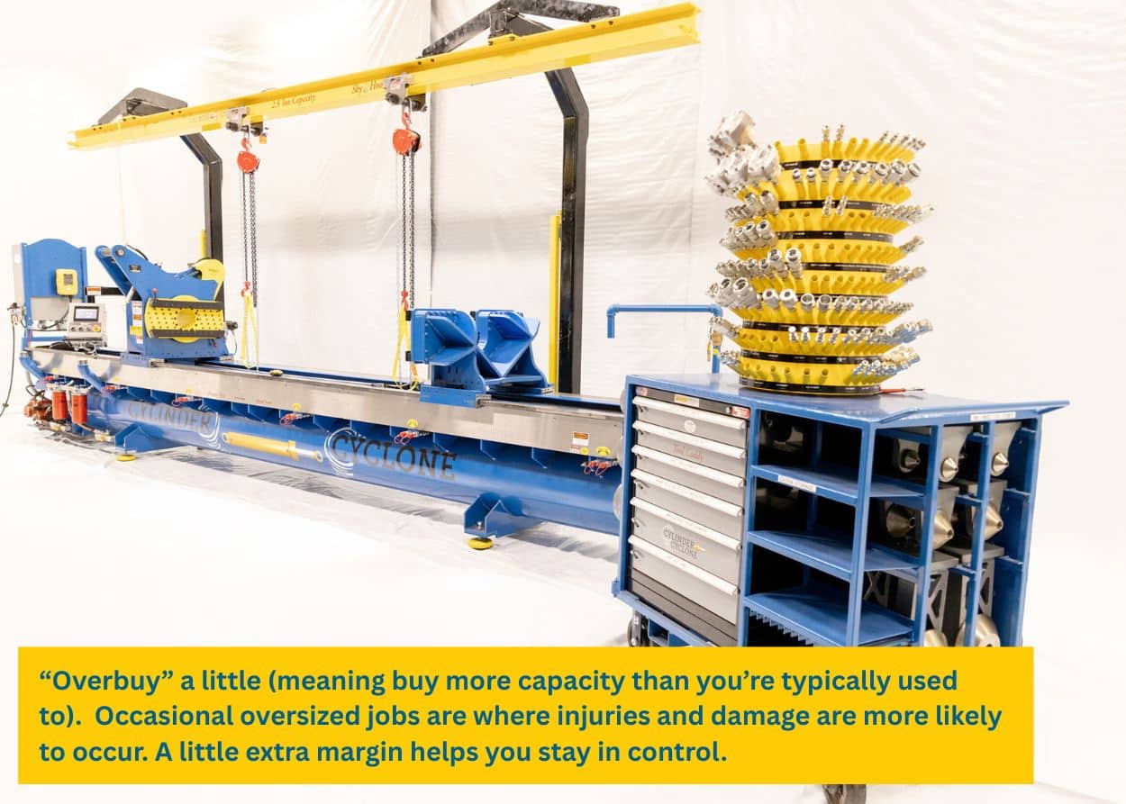 Large blue and yellow hydraulic cylinder repair bench setup with hoists, clamps, and tool storage in a clean industrial workspace. Caption: “Overbuy” a little (meaning buy more capacity than you’re typically used to). Occasional oversized jobs are where injuries and damage are more likely to occur. A little extra margin helps you stay in control.